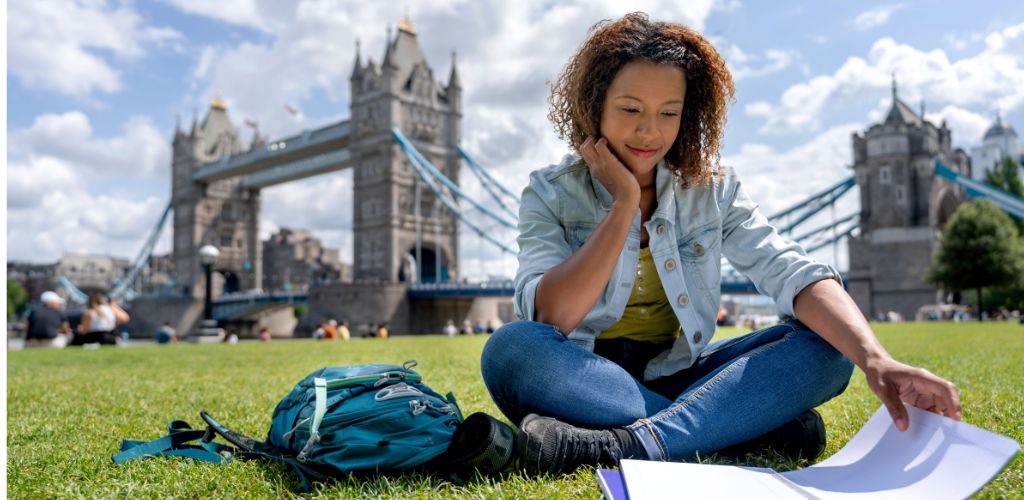 A happy Nigerian student holding a "Fully Funded" scholarship award letter in front of a UK university building, symbolizing successful financial aid.